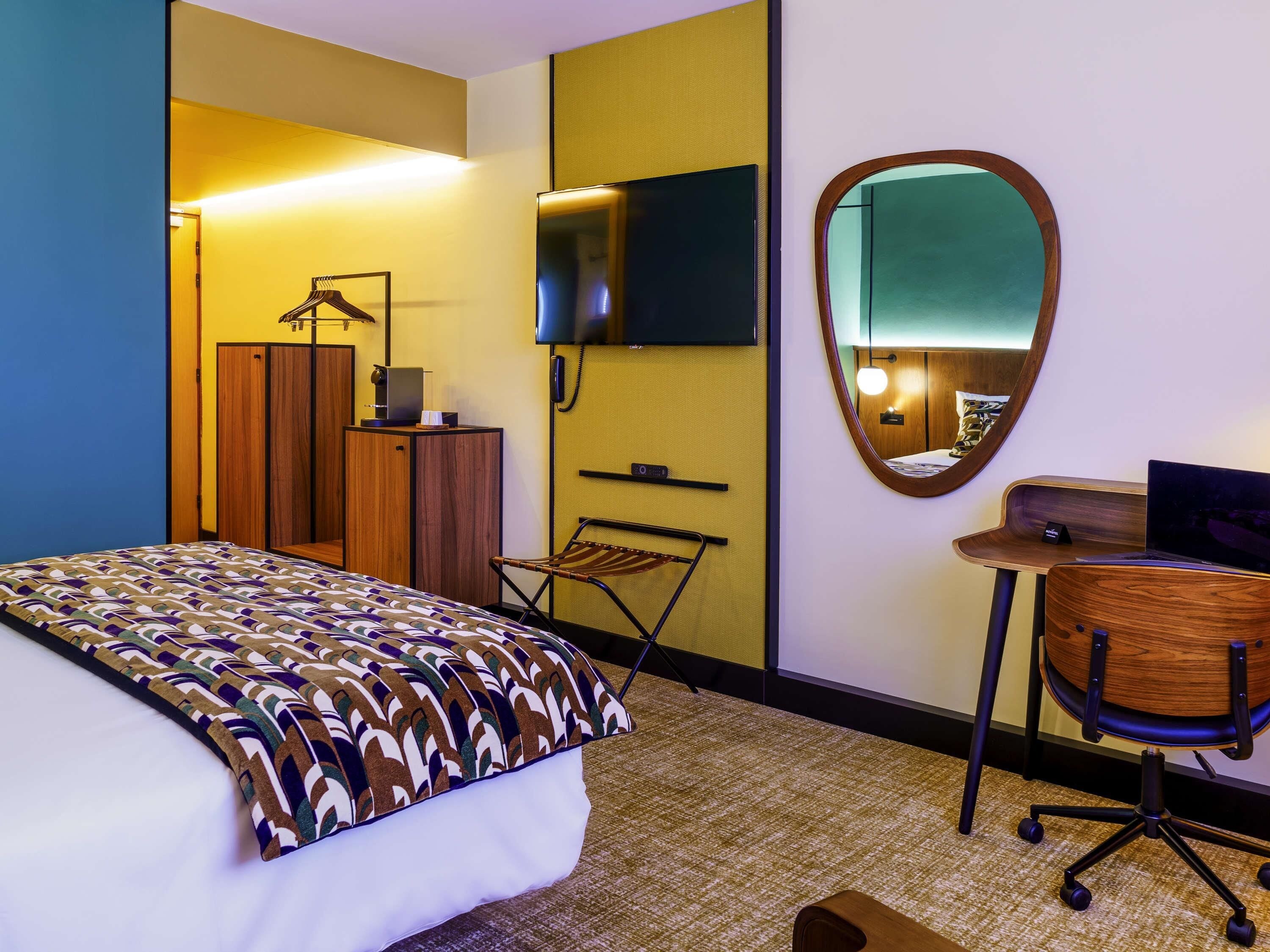 Une chambre d’hôtel équipée d’un lit, d’un bureau, d’une chaise, d’un miroir, d’une télévision et d’une armoire.