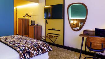 Una habitación de hotel con cama, escritorio, silla, espejo, televisor y armario.