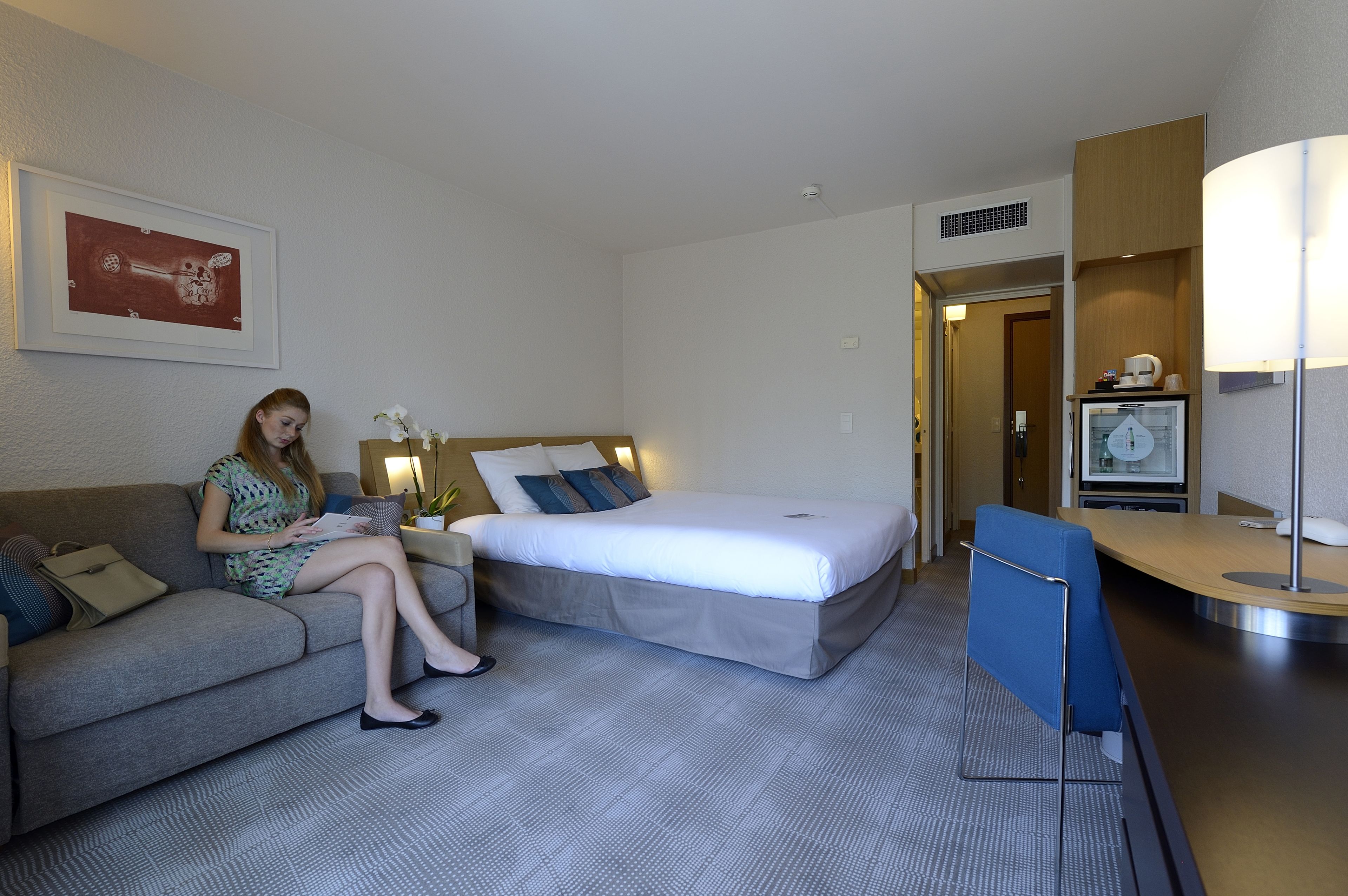 Quarto de hotel com cama, sofá, escrivaninha e abajur.