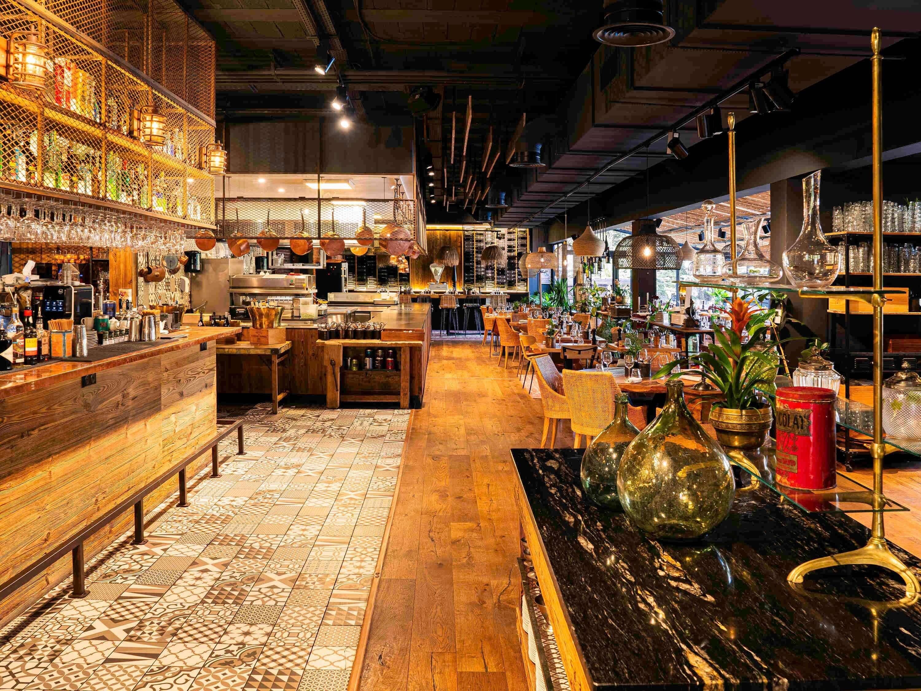 A bar area with wooden flooring, a counter with various bottles, and hanging lights.