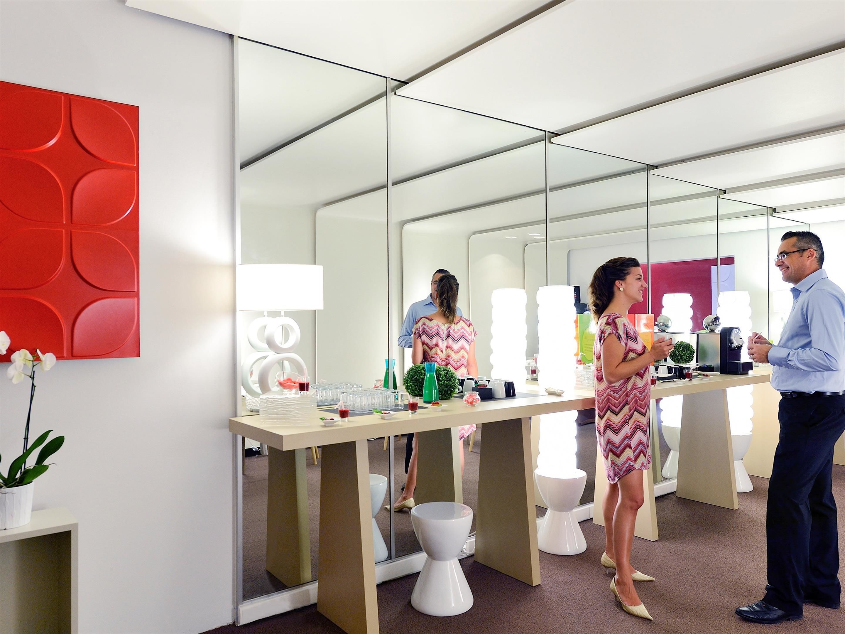 Een moderne kantoorruimte met spiegelwanden, een rode geometrische wanddecoratie en een balie met verschillende objecten.