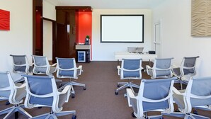 A conference room with a large screen, multiple chairs, a desk with a laptop, and a red accent wall. - Novotel Avignon Nord (Sorgues)