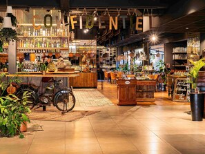 A cozy cafe interior with wooden furniture, a bicycle, and various plants. - Novotel Avignon Nord (Sorgues)