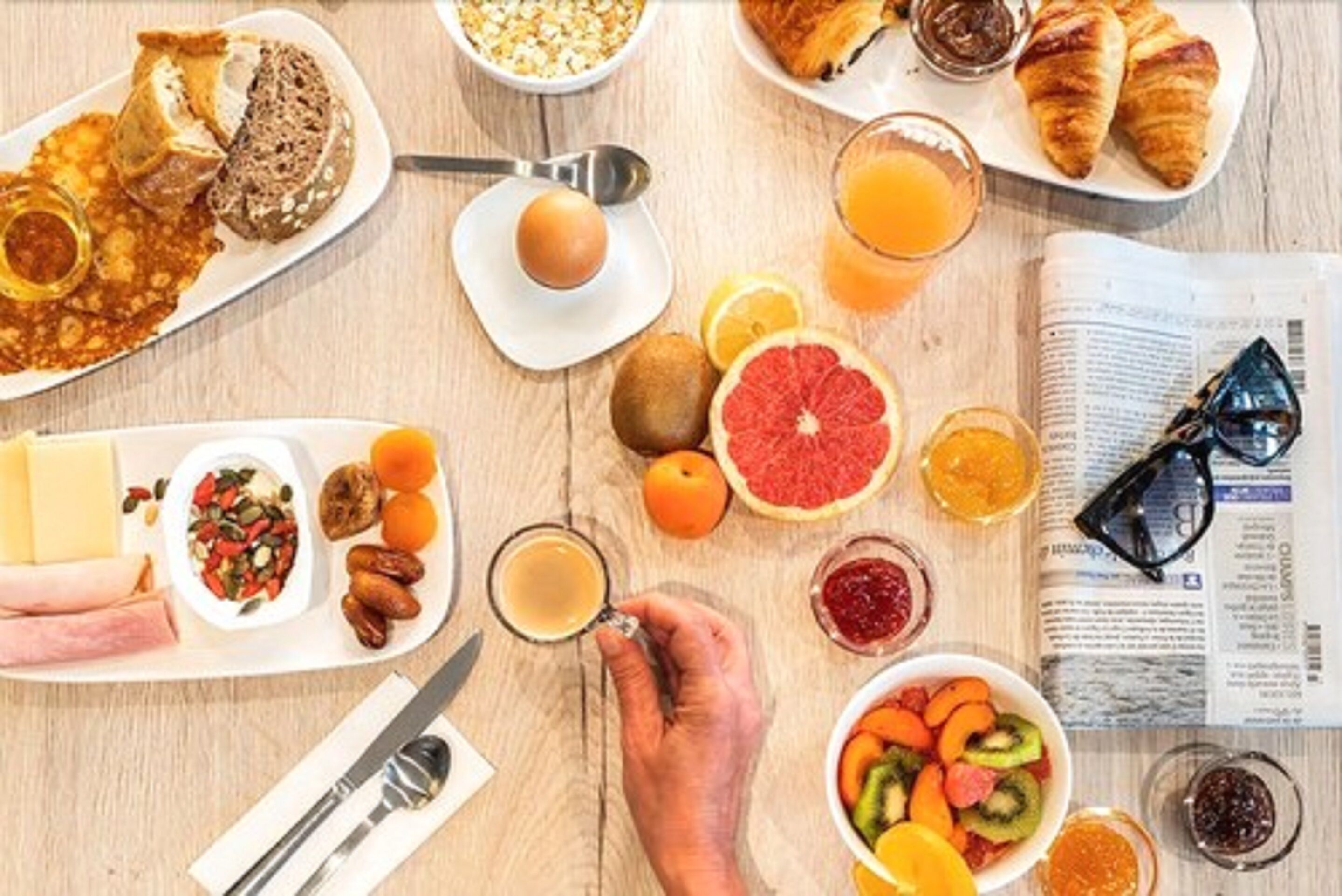 Una mesa de desayuno con diferentes alimentos, un periódico y un par de gafas.