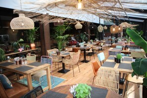 Un restaurant avec des tables et des chaises en bois, des plantes en pot et des luminaires suspendus.