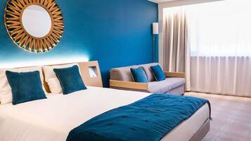 Una habitación de hotel con una cama grande, un sofá, un espejo montado en la pared y una ventana con cortinas.