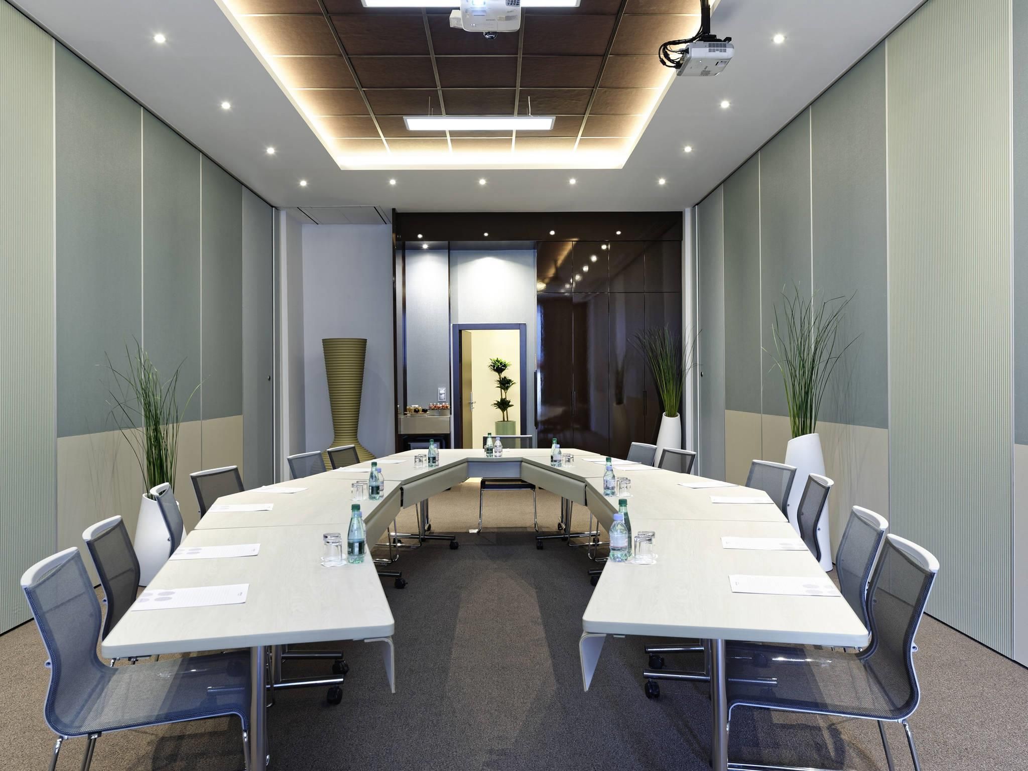 Une salle de conférence équipée d’une longue table, de chaises et de projecteurs fixés au plafond.