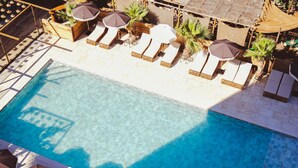 A clear blue pool with sun loungers and umbrellas, surrounded by palm trees and wooden structures. - Novotel Avignon Nord (Sorgues)