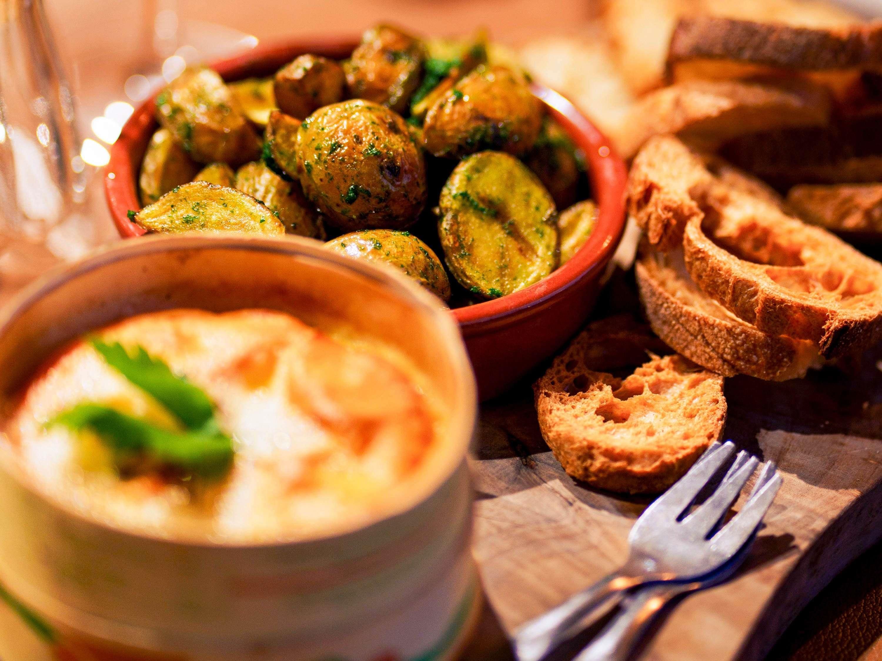 A bowl of roasted potatoes, a bowl of soup, and slices of bread on a wooden table.