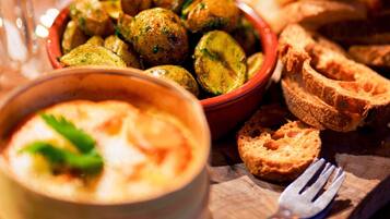 A bowl of roasted potatoes, a bowl of soup, and slices of bread on a wooden table.