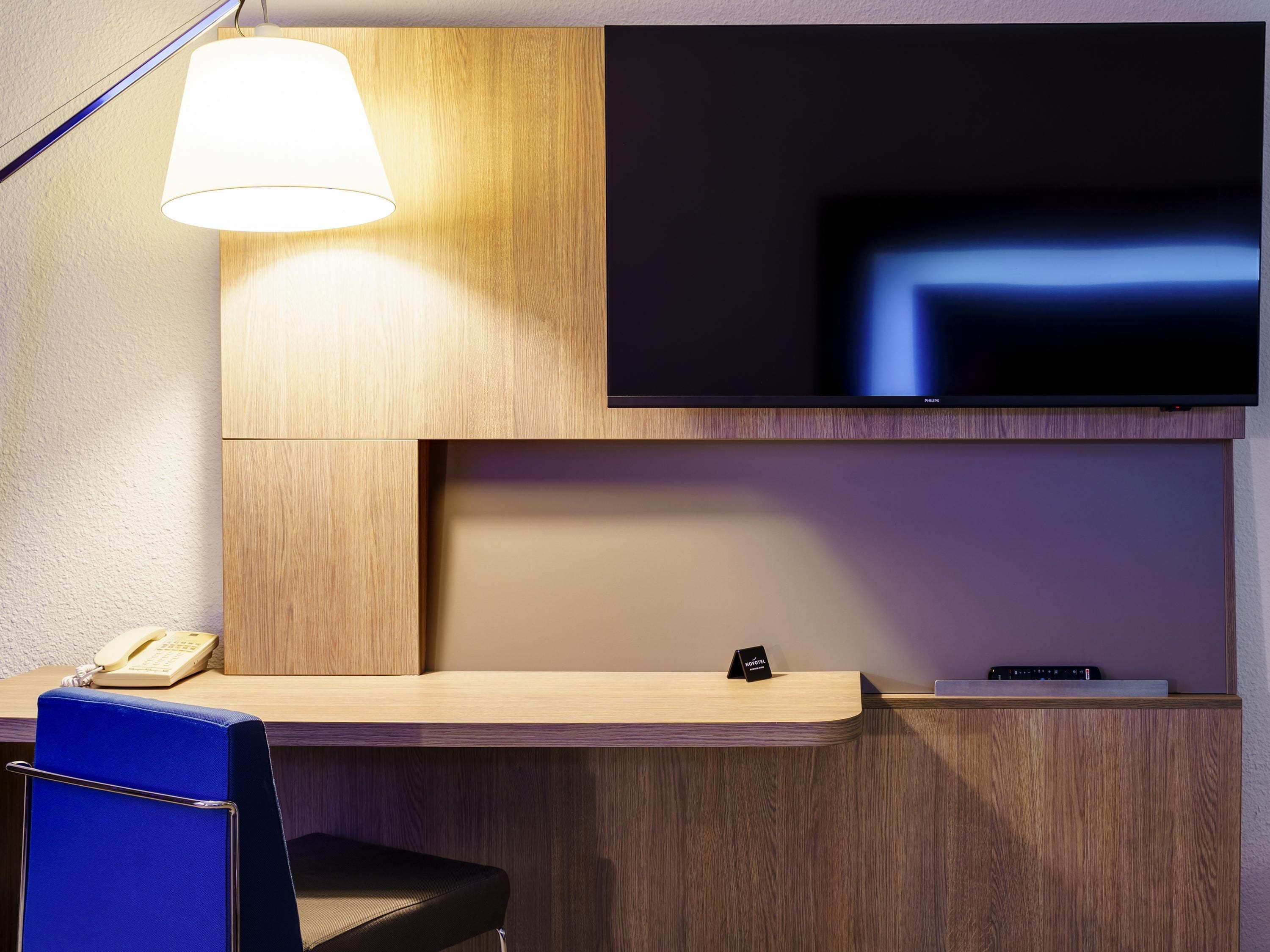 Een hotel receptie met een houten receptiebalie, een flatscreen televisie erboven, een telefoon en een blauwe stoel.