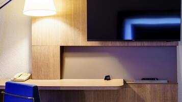 Een hotel receptie met een houten receptiebalie, een flatscreen televisie erboven, een telefoon en een blauwe stoel.