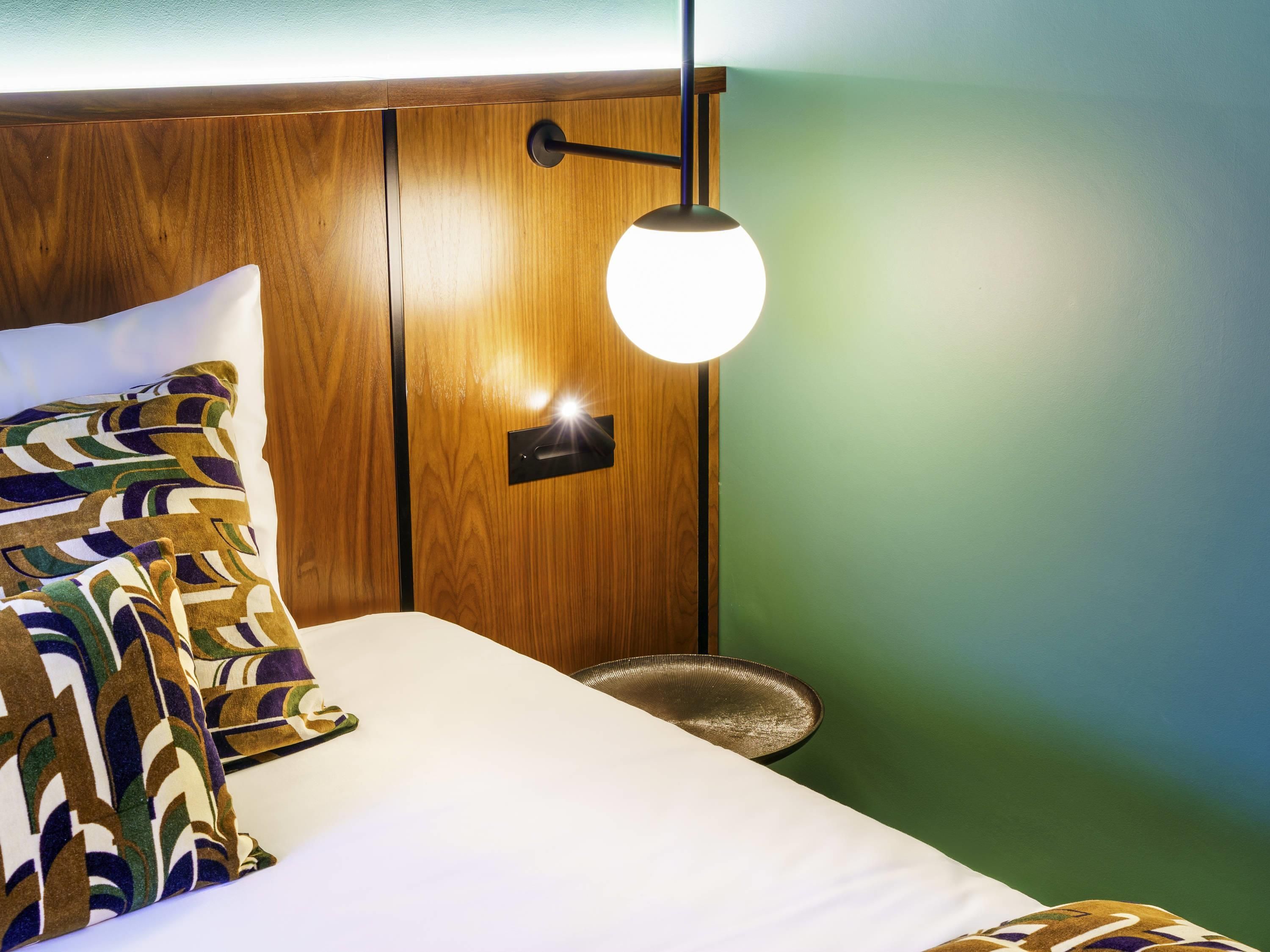 Een bed met een gestreept kussen, een nachtkastje met een schaal en een wandlamp.