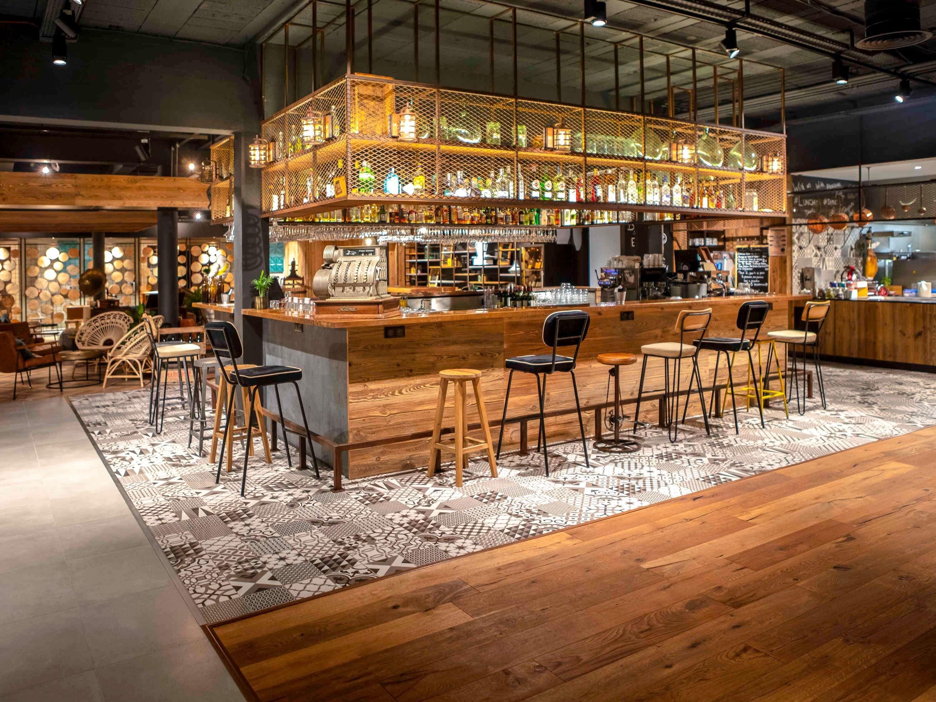 Zona de bar con mostrador de madera, taburetes y una alfombra estampada.