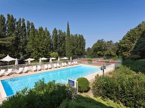A swimming pool with lounge chairs and umbrellas, surrounded by greenery and trees. - Novotel Avignon Nord (Sorgues)