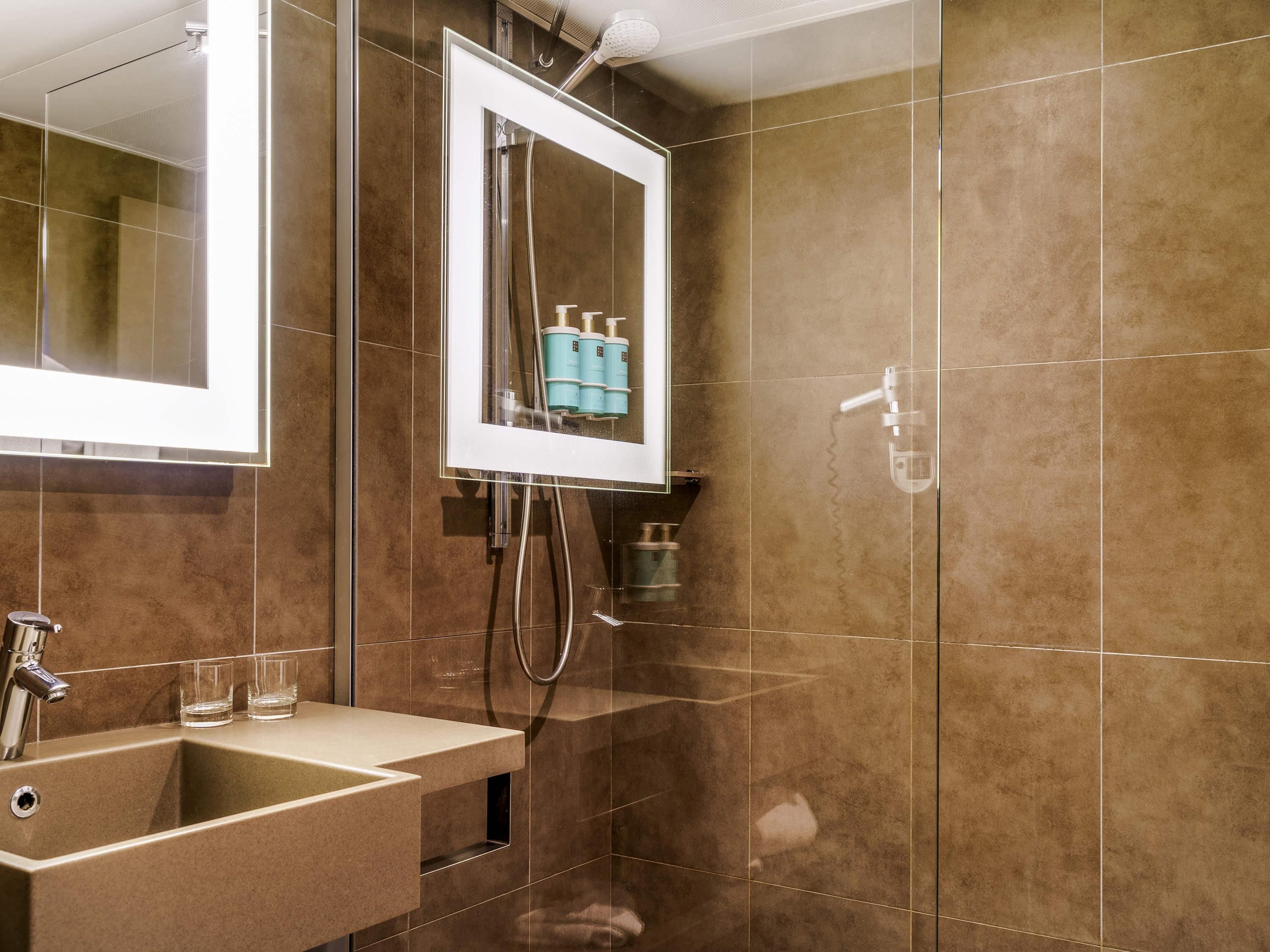 Ein modernes Badezimmer mit einer Duschkabine, einem Waschbecken mit Spiegel und einem wandmontierten Seifenspender.