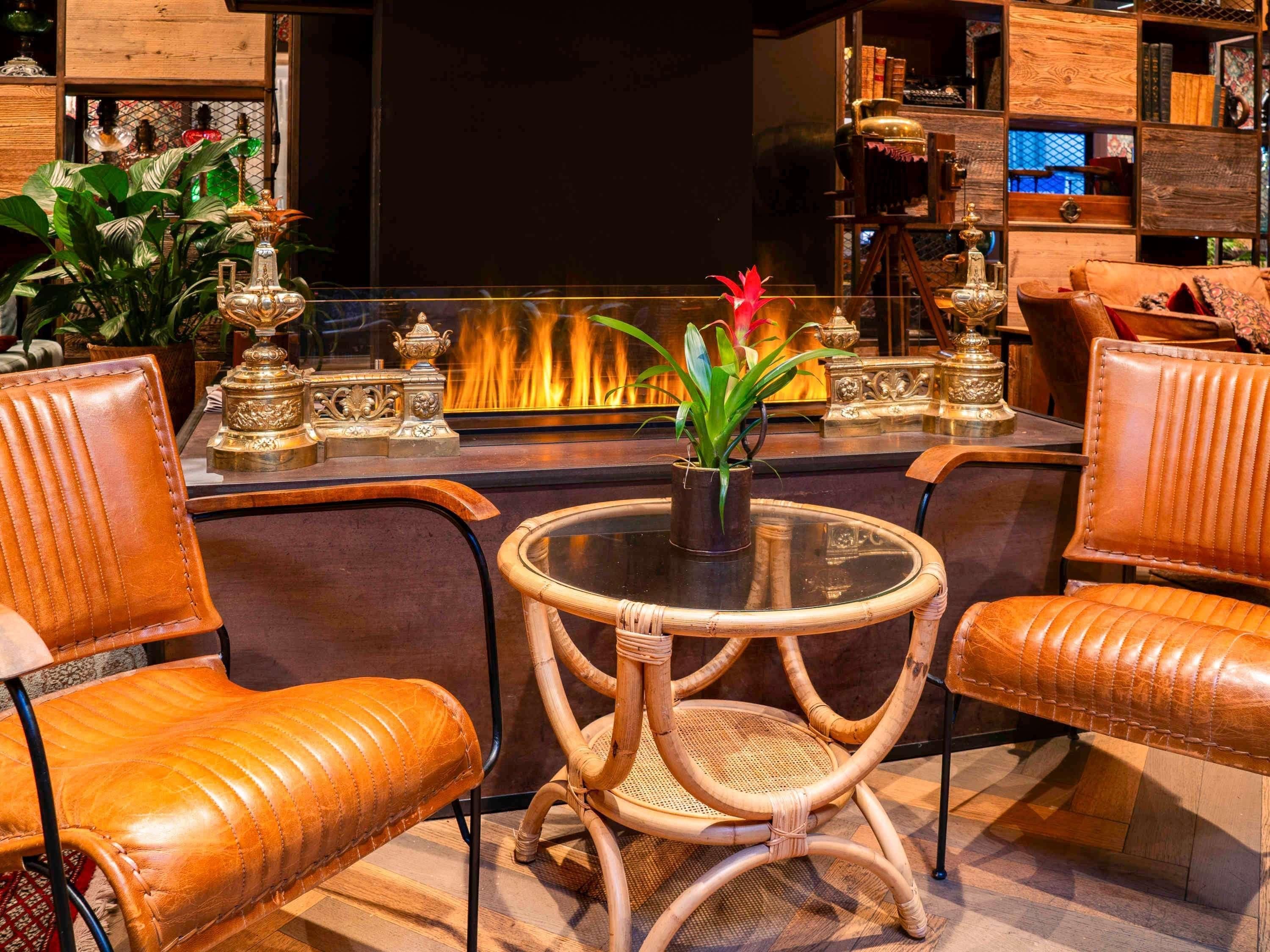 Ein gemütlicher Lounge-Bereich mit Ledersesseln, einem runden Tisch mit Glasplatte und einem dekorativen Kamin im Hintergrund.