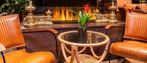 Ein gemütlicher Lounge-Bereich mit Ledersesseln, einem runden Tisch mit Glasplatte und einem dekorativen Kamin im Hintergrund.