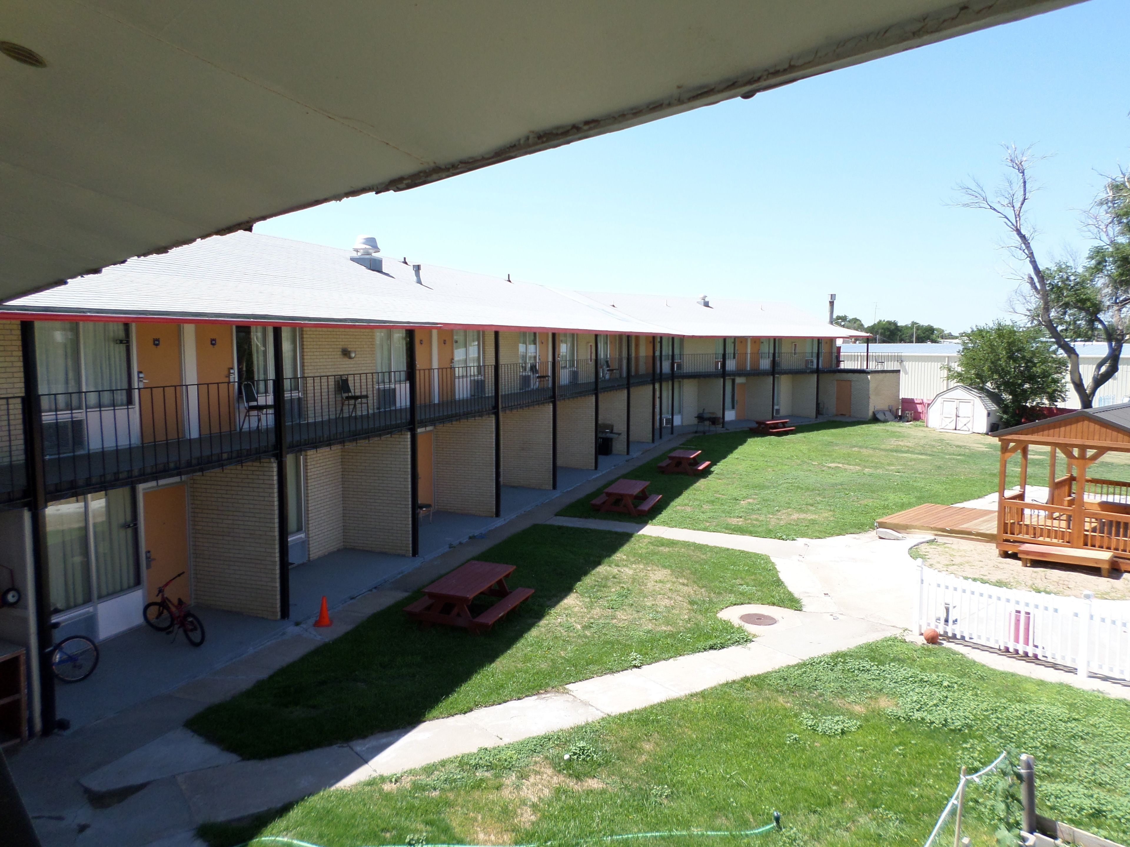Un motel amb una zona exterior coberta, taules de picnic i una petita construcció de fusta.