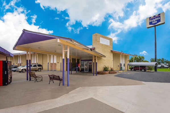 A Knights Inn with a covered parking area, outdoor seating, and a clear blue sky.