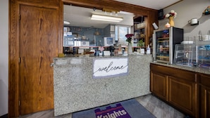 A reception area with a wooden door, a welcome sign, a counter with a computer, and a display case with items. - Travelodge by Wyndham Oakley (Oakley)