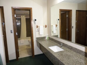 A bathroom with a granite countertop sink, a large mirror, and a shower area visible through an open door.