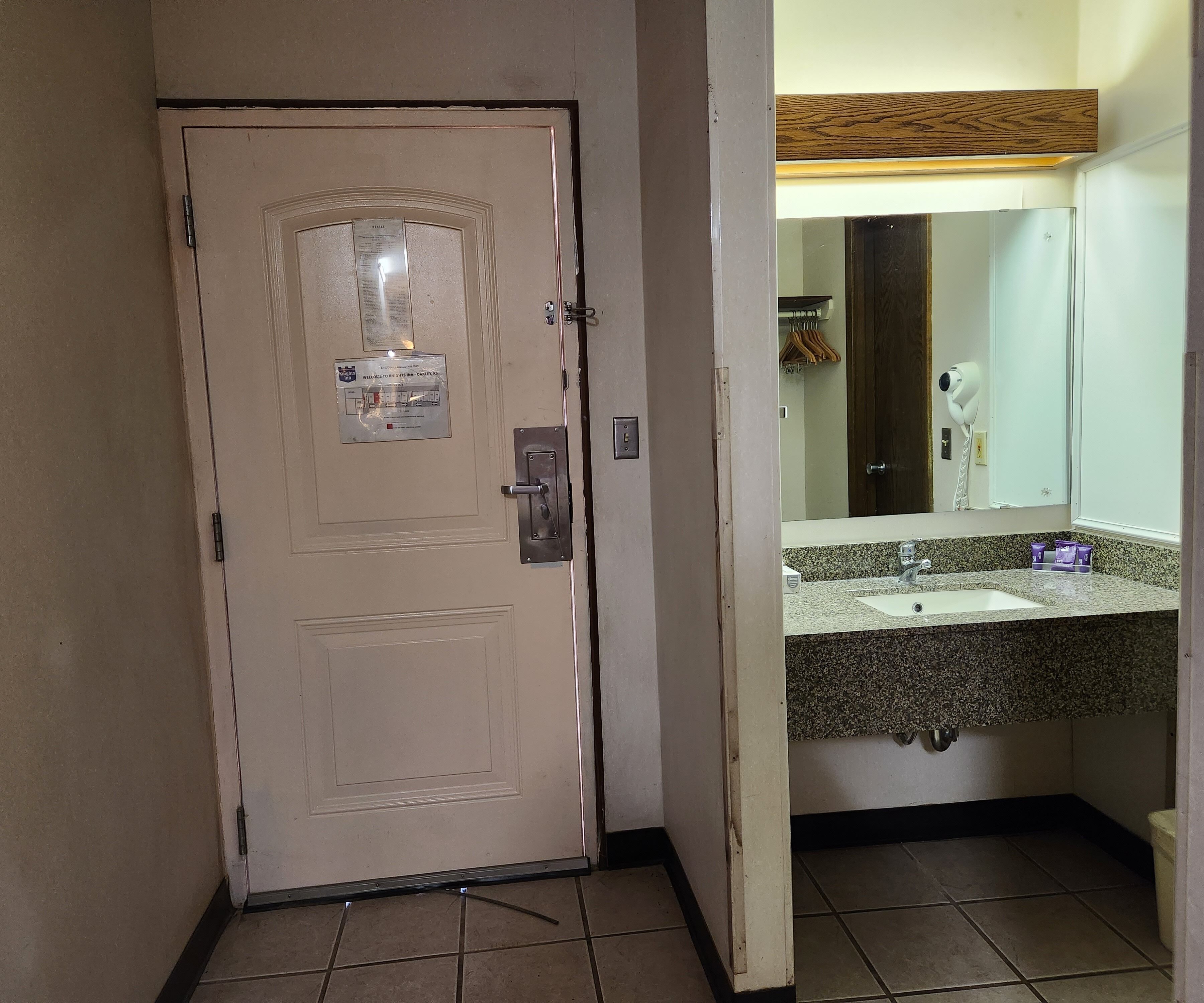 Habitación de hotel con una puerta color crema, un espejo pequeño sobre un lavabo y un perchero.