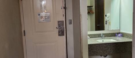 Habitación de hotel con una puerta color crema, un espejo pequeño sobre un lavabo y un perchero.