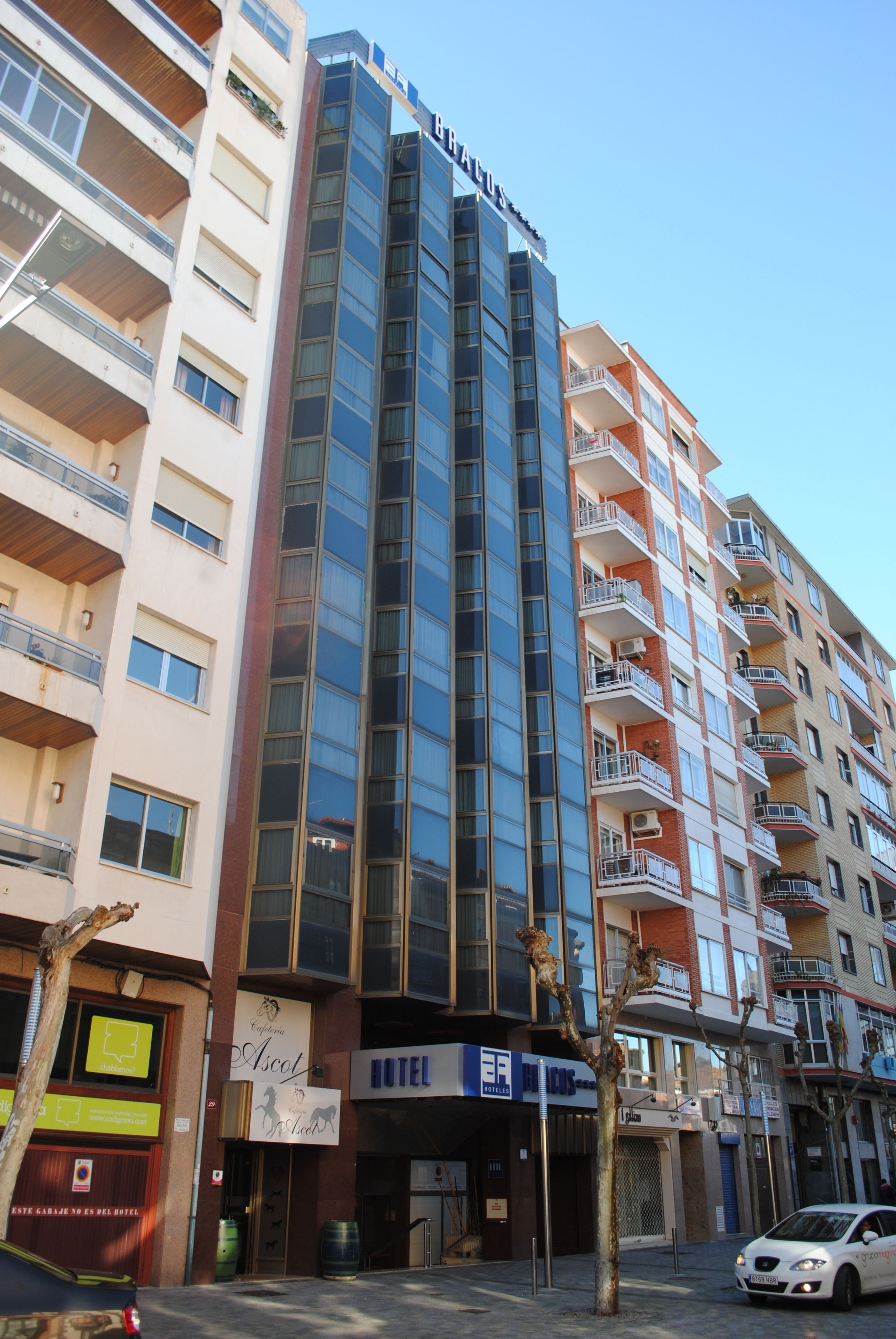 Un hotel de varios pisos con fachada de vidrio moderna, balcones y un cartel visible que dice 'Hotel Ascut'.