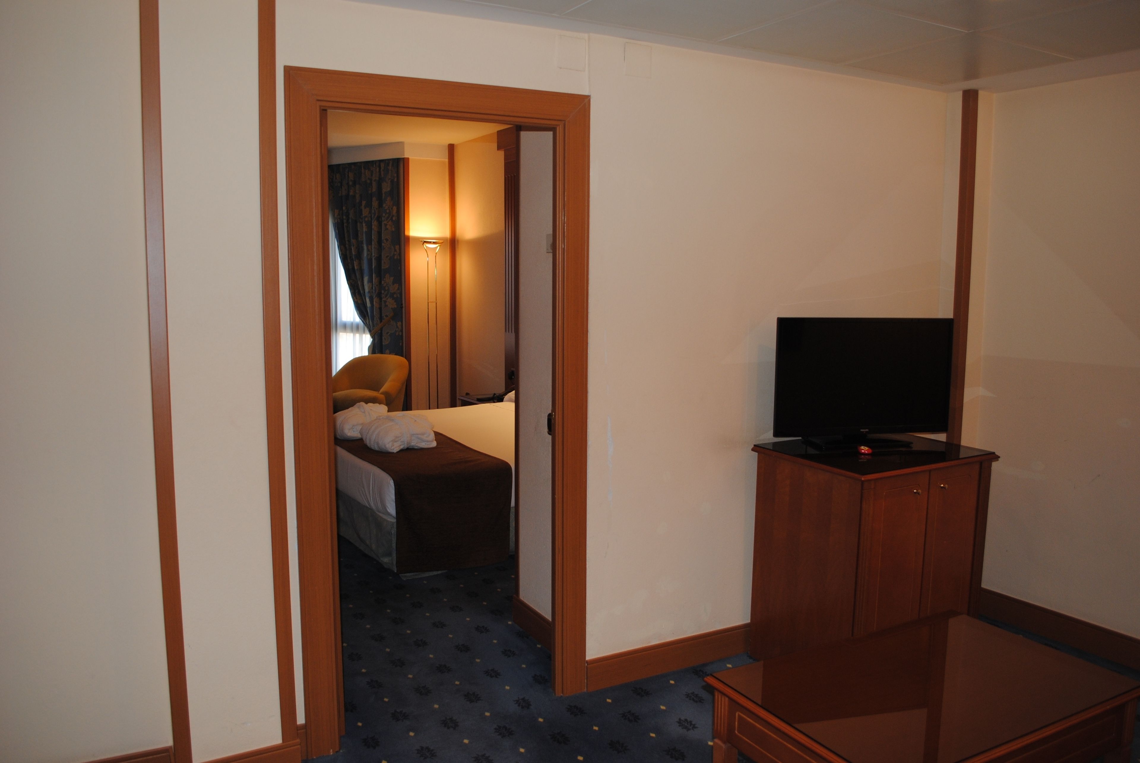 A hotel room with a bed, a television on a wooden cabinet, and a door leading to another room.