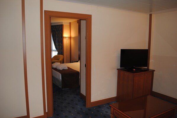 A hotel room with a bed, a television on a wooden cabinet, and a door leading to another room. - Hotel Los Bracos (Logroño)