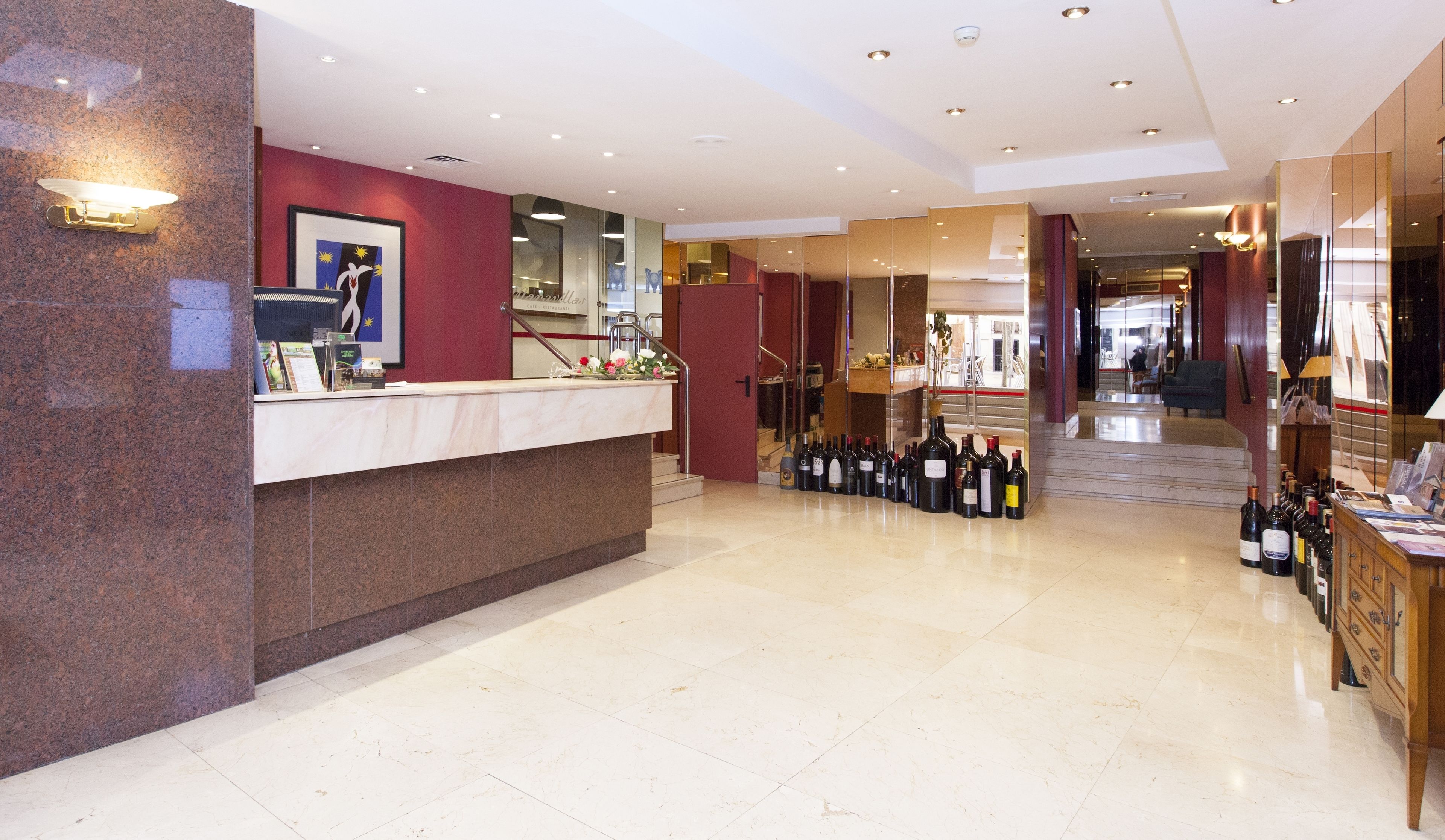 A hotel lobby with a reception desk, a display of wine bottles, and a staircase leading to another area.