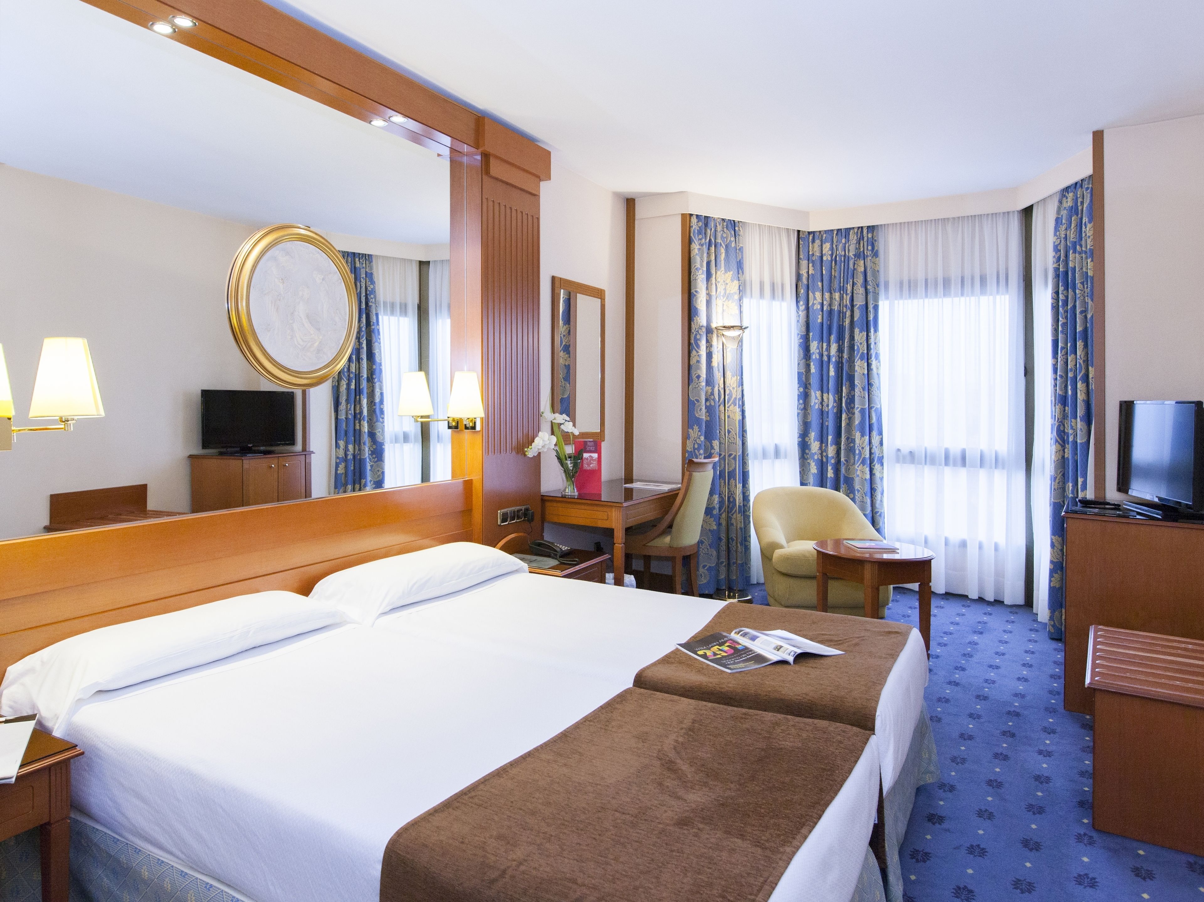 Ein Hotelzimmer mit einem großen Bett, einem Schreibtisch, einem Sessel, einem Fernseher und einem großen Spiegel.