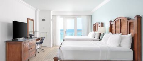 A hotel room with a wooden bed, a TV, a desk, and a view of the ocean.
