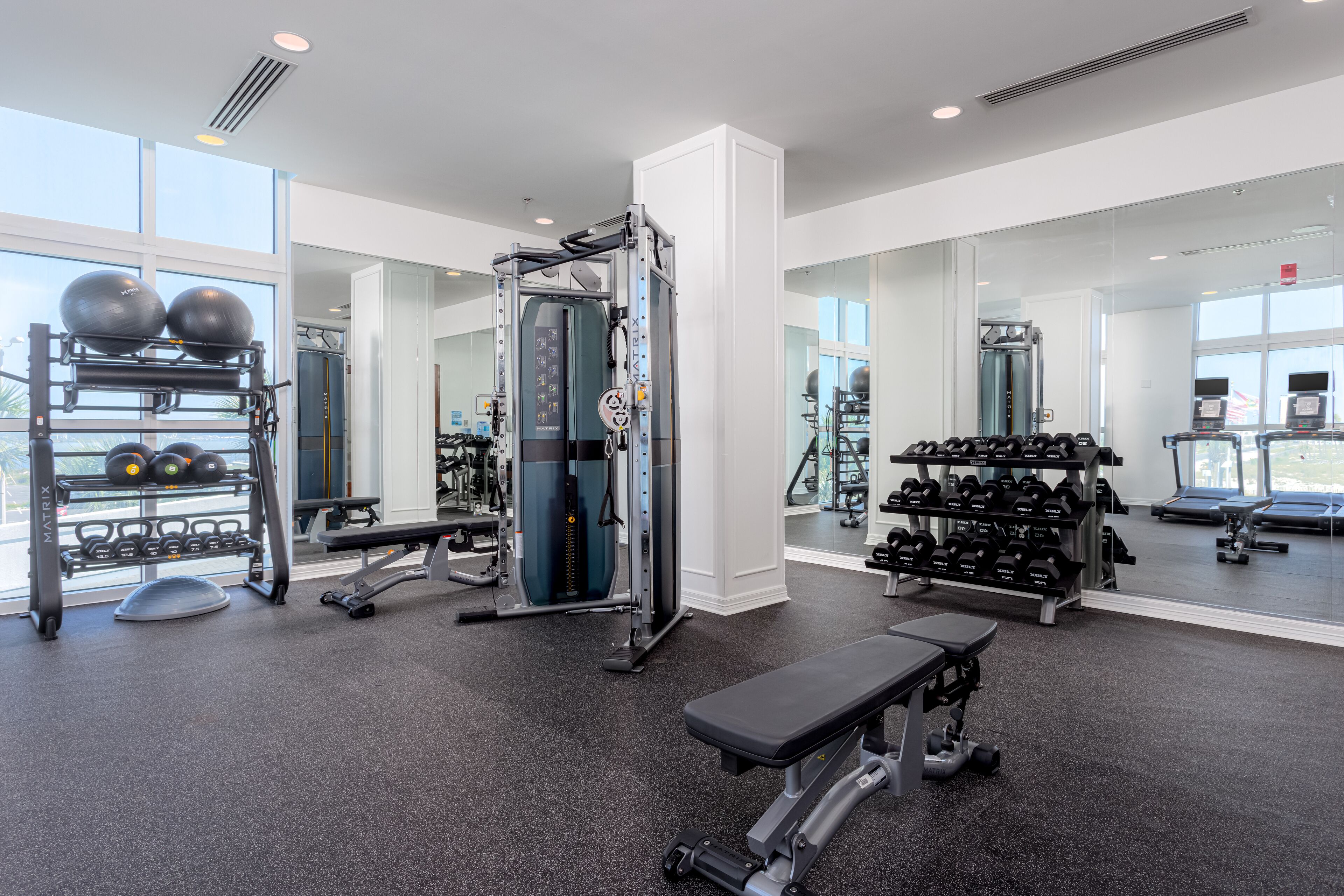 A modern gym with various exercise equipment, including a squat rack, bench, and free weights.