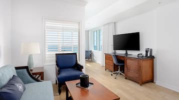 Una habitación de hotel moderna con sofá, escritorio, televisión y ventana con persianas.