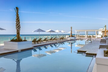 Una piscina al aire libre, sombrillas, sillones reclinables de piscina