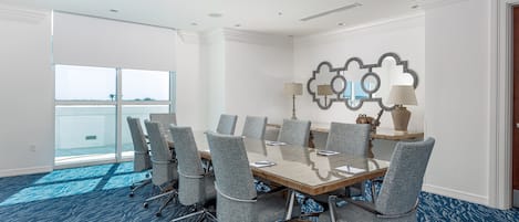 A conference room with a glass table, grey chairs, a patterned carpet, and a large window with a view.
