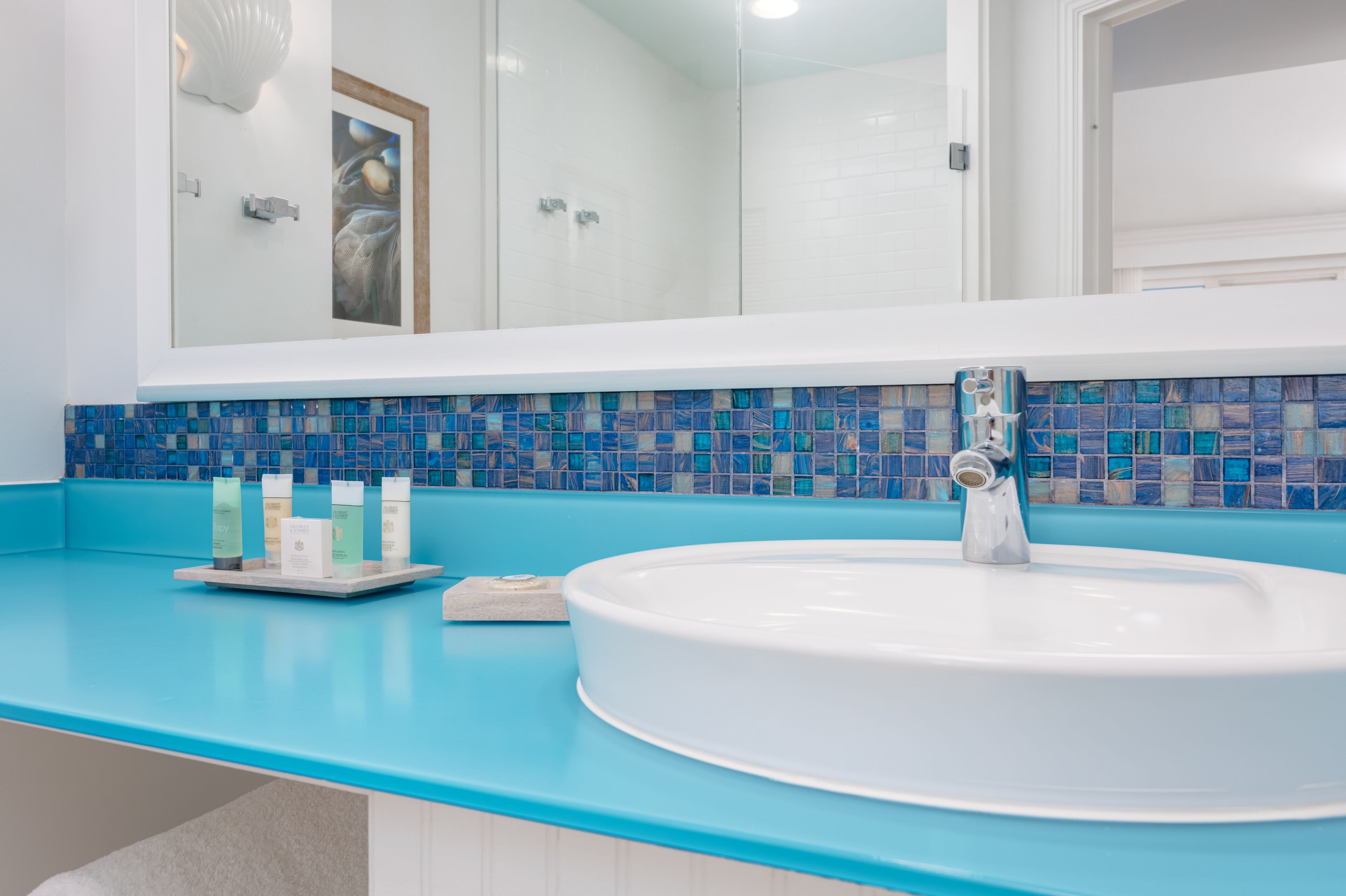 A bathroom with a large mirror, a white sink, and a blue tiled backsplash.