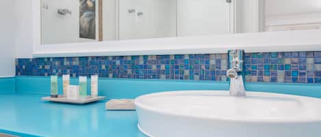 A bathroom with a large mirror, a white sink, and a blue tiled backsplash.