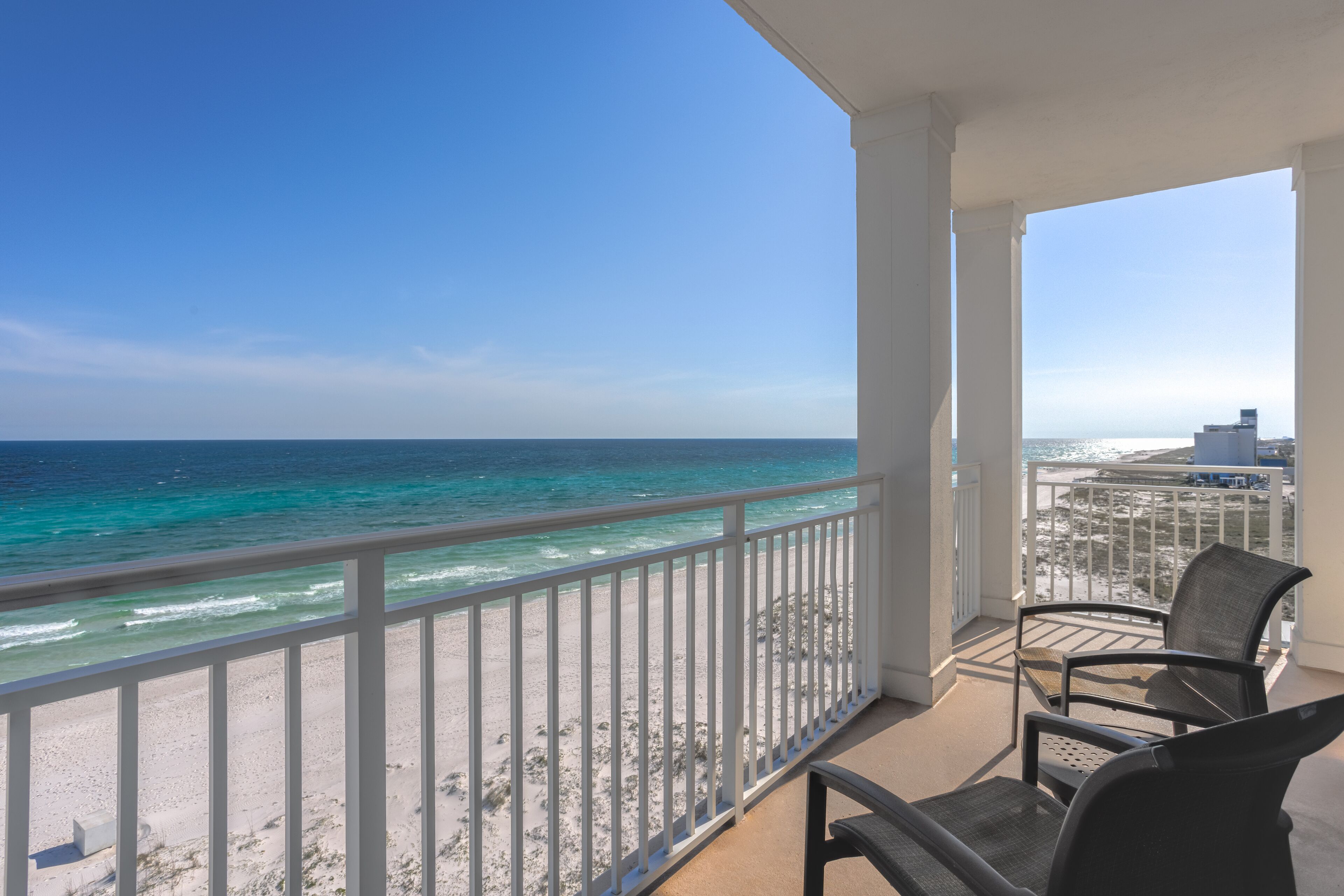 A balcony with a view of the ocean and beach, featuring two chairs and a white railing.