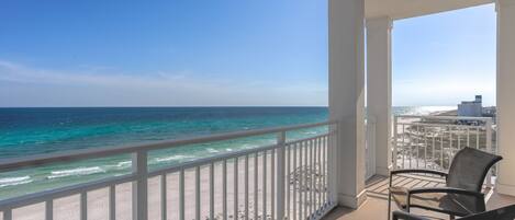 A balcony with a view of the ocean and beach, featuring two chairs and a white railing.