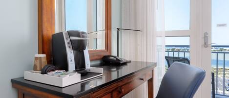 Une chambre d’hôtel avec un bureau en bois, une machine à café, un téléphone et une vue sur la mer depuis la porte-fenêtre donnant sur le balcon.
