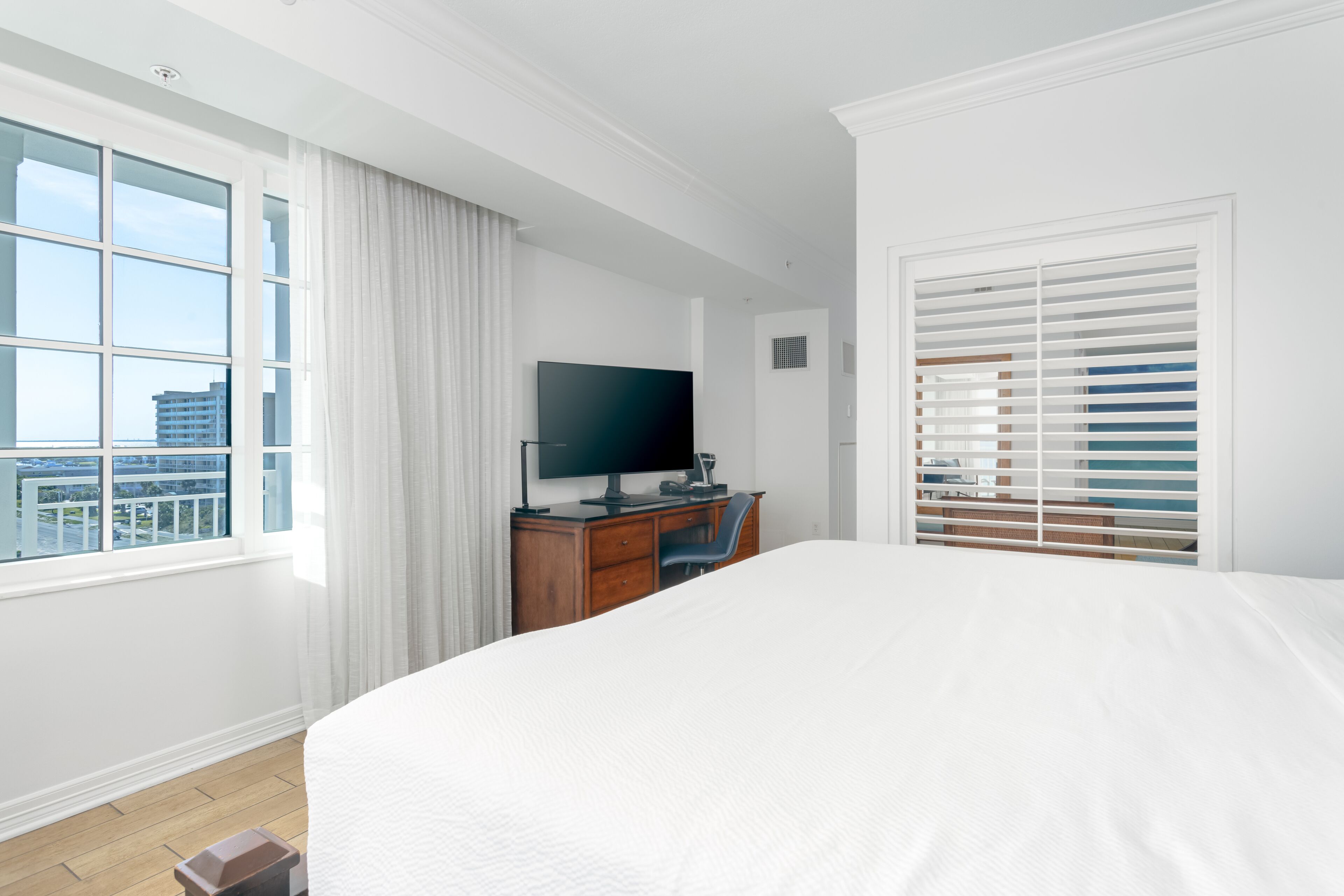 A hotel room with a large bed, a desk with a computer, a TV, and a window with blinds.