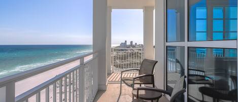 A balcony with a view of the beach and ocean, furnished with chairs and a table.