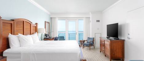 Habitación de hotel con una cama grande, cabecera de madera, televisor, escritorio con lámpara, silla y vistas al balcón.