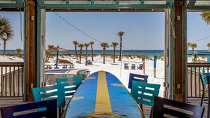 Um restaurante à beira-mar com vista para o oceano, mesas ao ar livre e palmeiras.