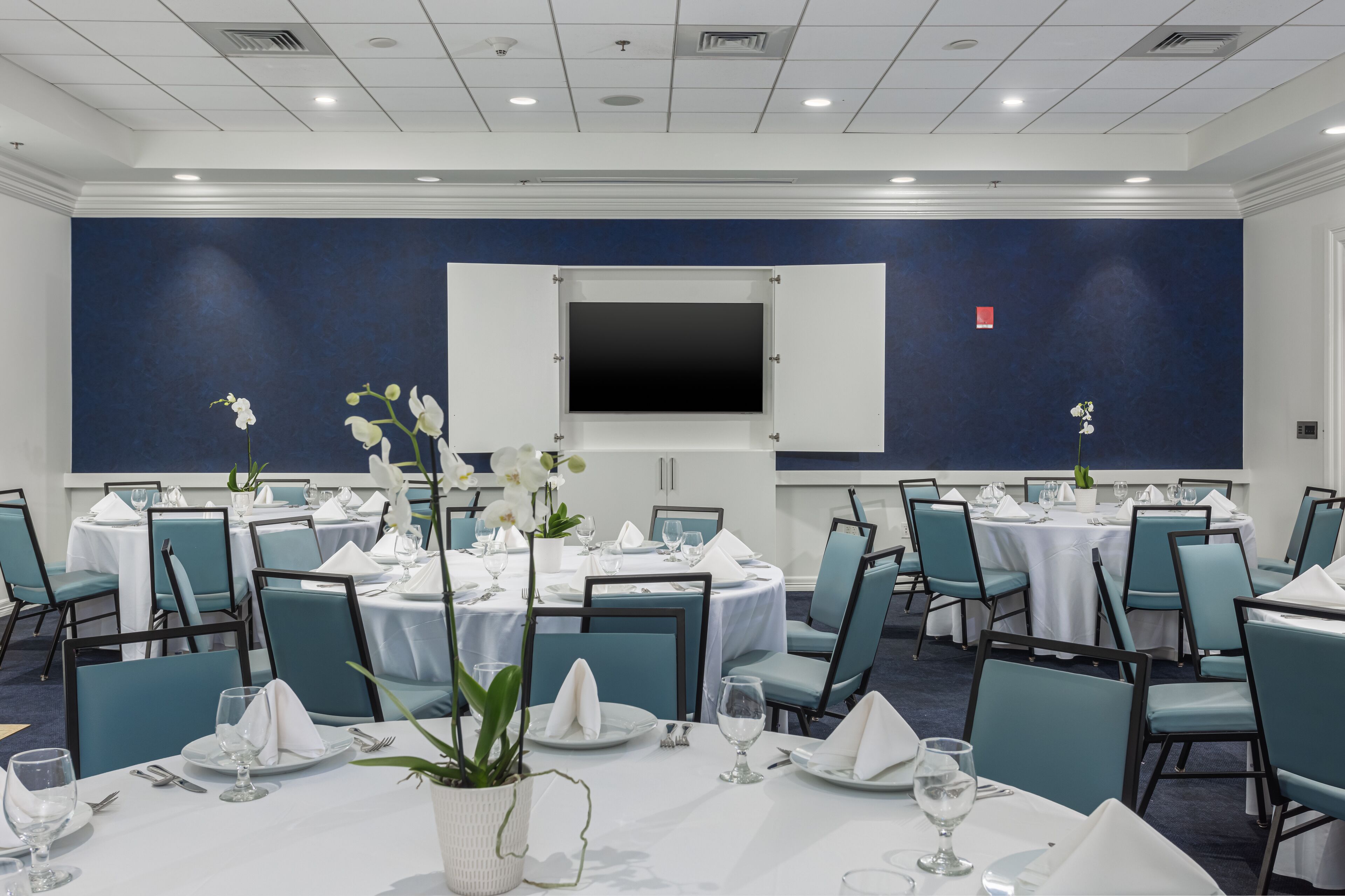 Un salón de conferencias con mesas redondas, sillas y una pantalla grande.