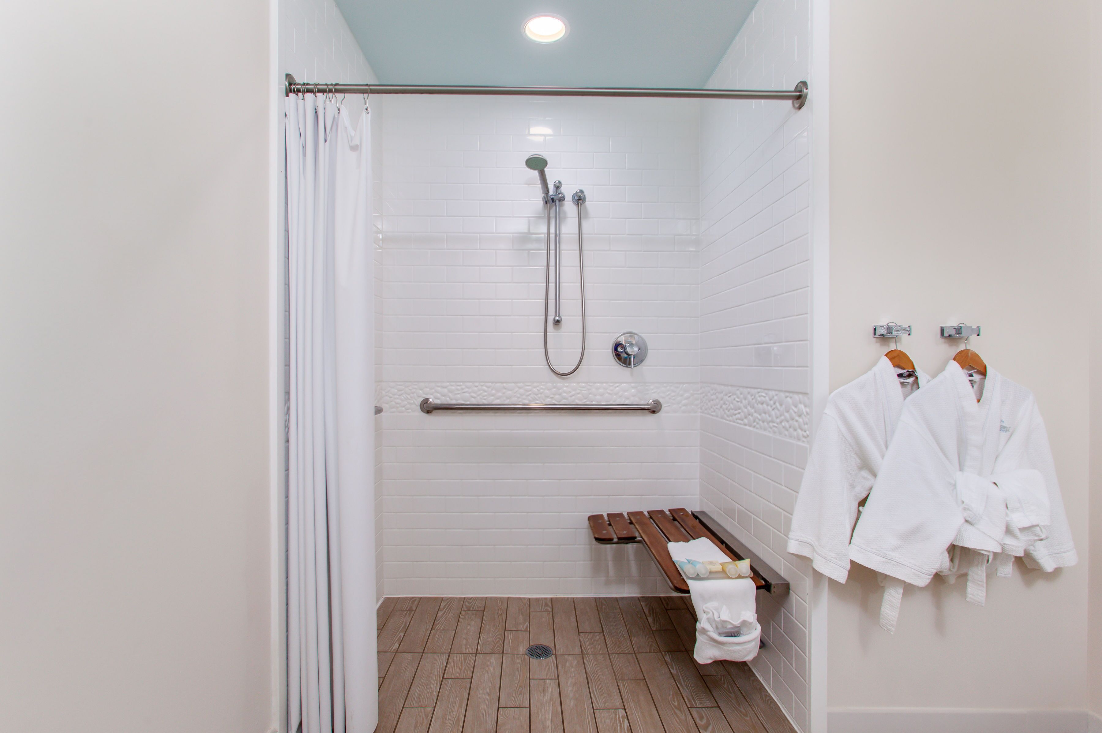 A shower area with a glass door, a bench, and two white robes hanging on hooks.