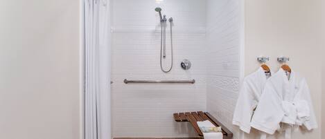 Área de chuveiro com porta de vidro, um banco e duas toalhas brancas penduradas em ganchos.